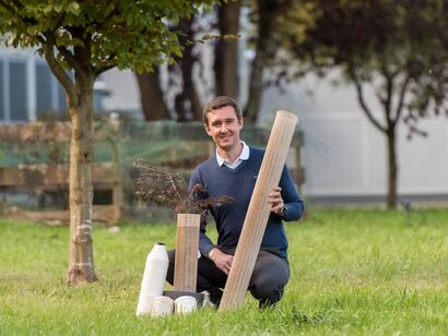Stephan Baz (Head of Staple Fiber Technologies) with the environmentally friendly tree cover in original size and as a demonstrator on a red maple. In the foreground: hybrid yarn variants made from flax or cotton. 
