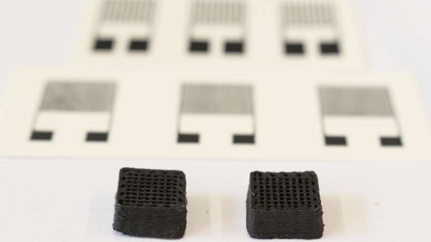 Novel material for printed circuits: Two test cuboids one centimeter wide from the 3D printer. The printed electronic sensors can be seen in the background. 
