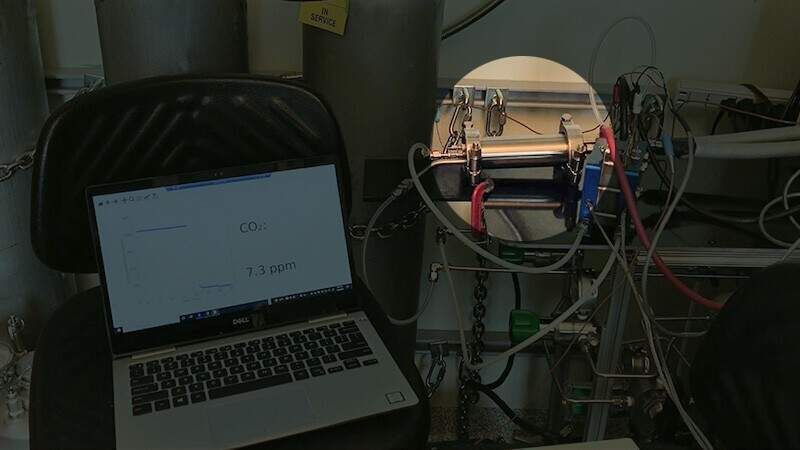 This picture shows the electrochemical system developed by the Yan group. Inside the highlighted cylindrical metal housing shown is the research team’s novel spiral wound module. As hydrogen is fed to the device, it powers the carbon dioxide removal process. Computer software on the laptop plots the carbon dioxide concentration in the air after passing through the module