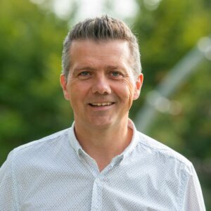 Portrait picture of happy-looking Tom Claessen in front of trees