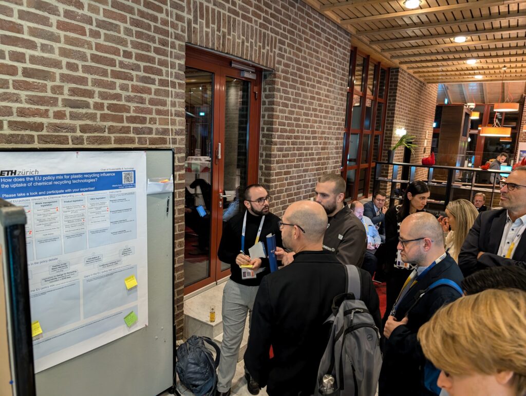 Conference participants intently review an elaborate scientific poster amid a backdrop of additional displays, underscoring the professional platform for showcasing innovative circular economy research.