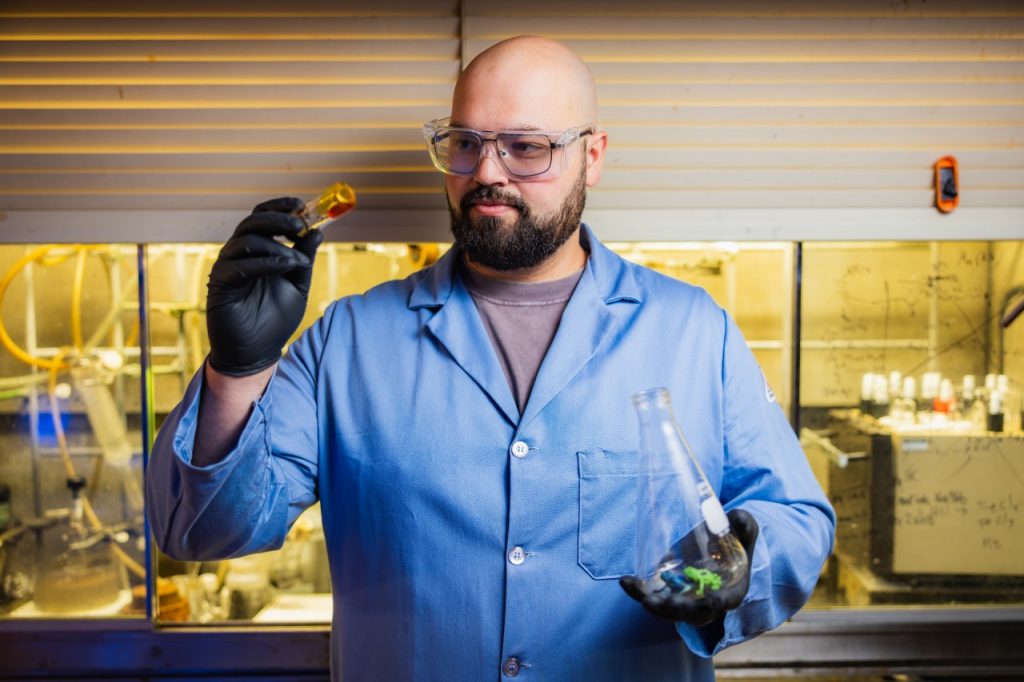 Graduate student Connor Thompson examines a sample of engine oil created from upcycled plastic waste in Greg Liu's lab. In his left hand he holds toy plastic frogs similar to those that were used in the process.